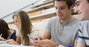 Student smiling and showing friend smartphone in lecture hall