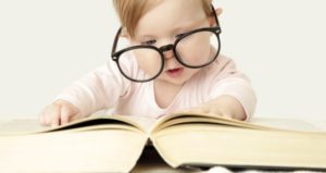 Baby with glasses looks at huge book