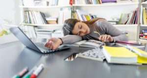 Student falls asleep at desk with computer, papers and books open