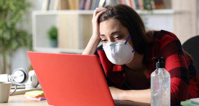 Student sits at computer with mask on looking defeated