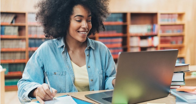 Student smiling at computer with notes and books surrounding her