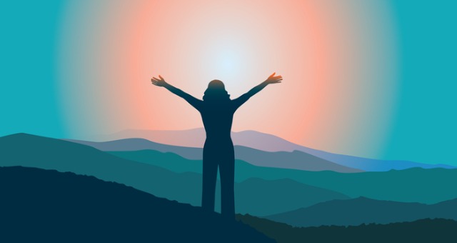 Person with hands in the air in success with sunset and mountains in background