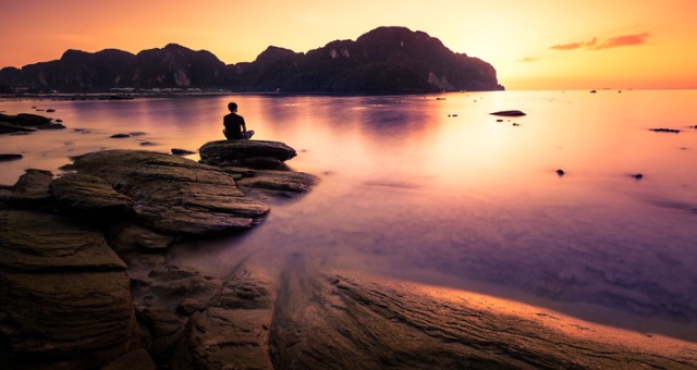 Person meditating on rocks with sunset