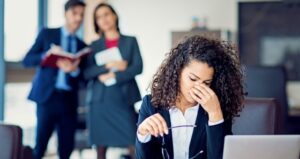 Woman sits in despair while two employees talk about her behind her back