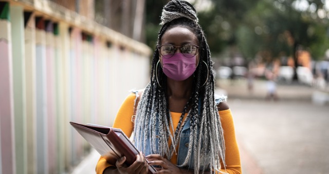 Woman holds books and smiles with face mask on