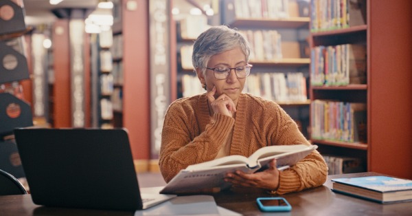 Woman thinking at library with laptop and books