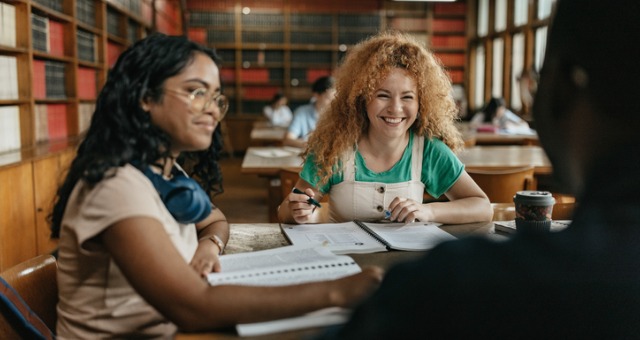 Students sit at table in library and study and laugh together