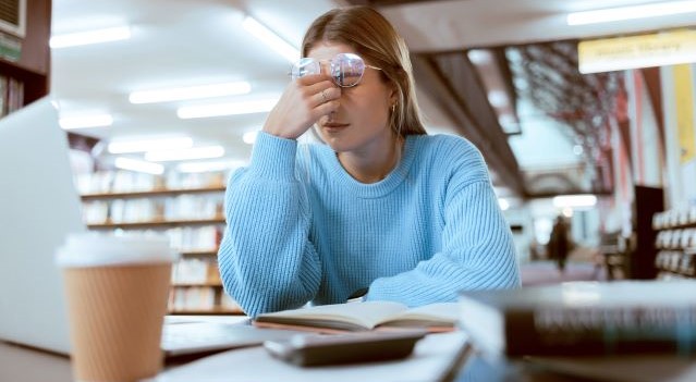 Student in library with hands to face, stressed with coffee