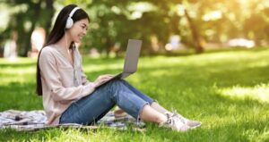 Student sitting outside on laptop with headphones and in sunshine