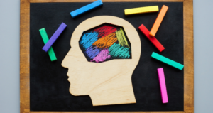 picture of a wooden face with a colorful brain, on a chalkboard with colorful chalk around it