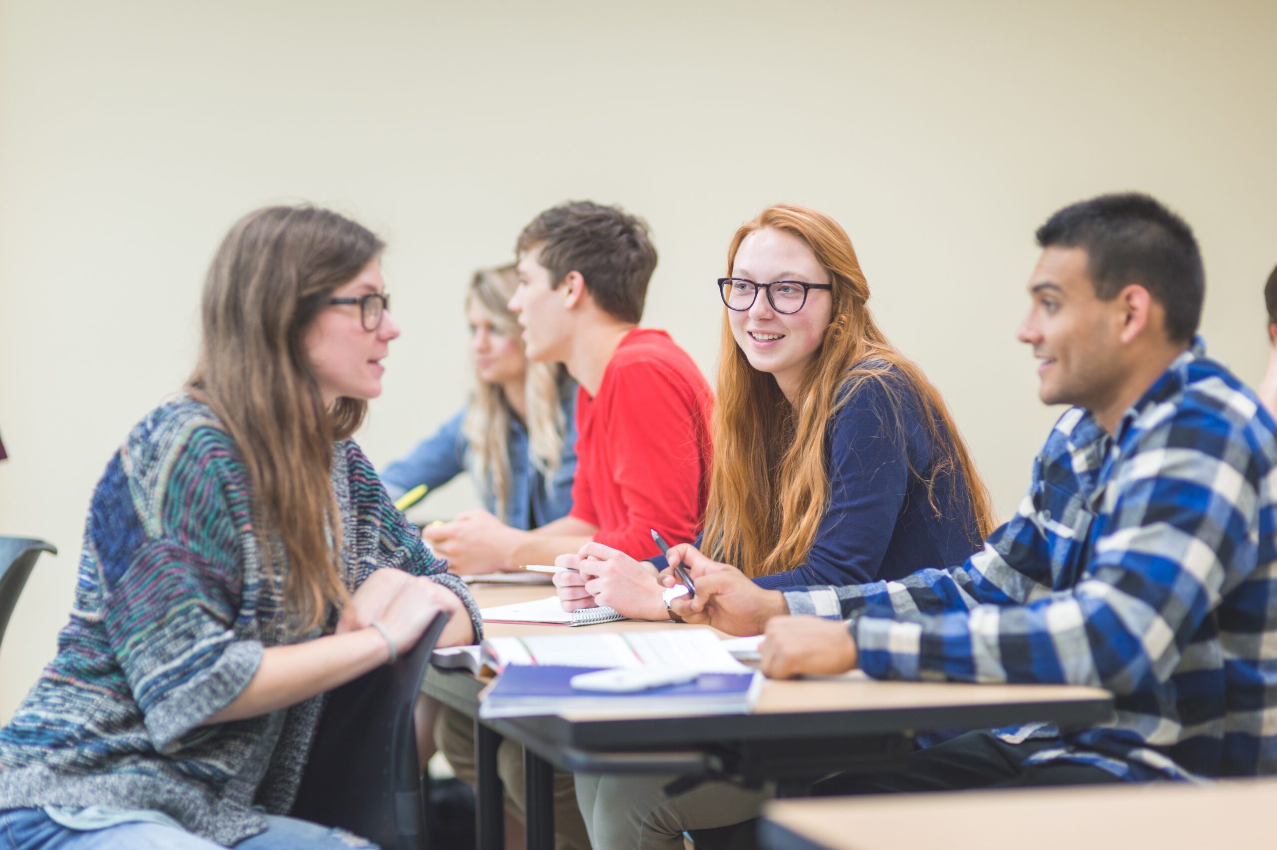 Students in university lecture hall study together. Several students are working and discussing the assignment together. One has her chair turned around and is working with the two students sitting behind her.