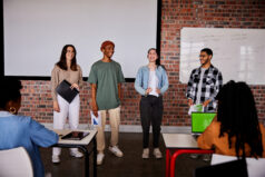 Group of diverse students laughing while giving a presentation to their classmates during a lesson at a school