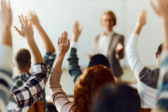 Back view of large group of high school students raising their hands to answer the professor's question on a class at high school.