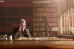 Displeased senior lawyer reading problematic rules of law in a book at library.