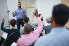 Middle Eastern mid adult man teacher talking teaching leading discussion with students hand raised in training seminar in school classroom for education training