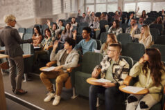 Large group of happy university students raising their hands to answer the professor's question on a class in amphitheater.