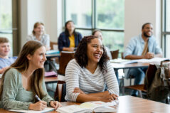 Joyful Pedagogy - A multiracial group of students smile and laugh during class.