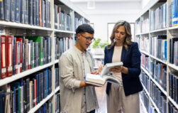 Teacher helping a Latin American college searching for a book at the library for research project - education concepts