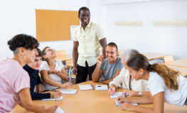African american male teacher teaches with kindness with happy students of different ages, conducts higher education classes at round table in the classroom