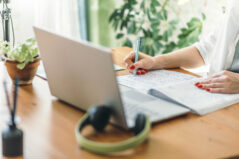 Educator working at desk with notes and laptop, reflecting on evaluations for course improvement.
