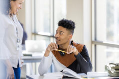 Young man talks with teacher, holding pencil; casual setting, selective focus. Building rapport. Student engagement. Learning names.