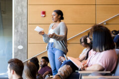 A mid adult African American female college student gestures while giving an oral report during class.