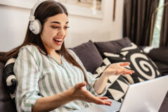 Young woman student sitting on the sofa happily engaged and participating in online class