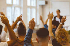 Rear view of male and female students answering during lecture. Women and men are raising hands while sitting in classroom. They are in university, college.
