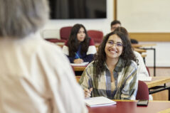 Over the shoulder view with focus on young woman sitting in front row of college classroom, enjoying the lecture and taking notes. Student-centered learning.