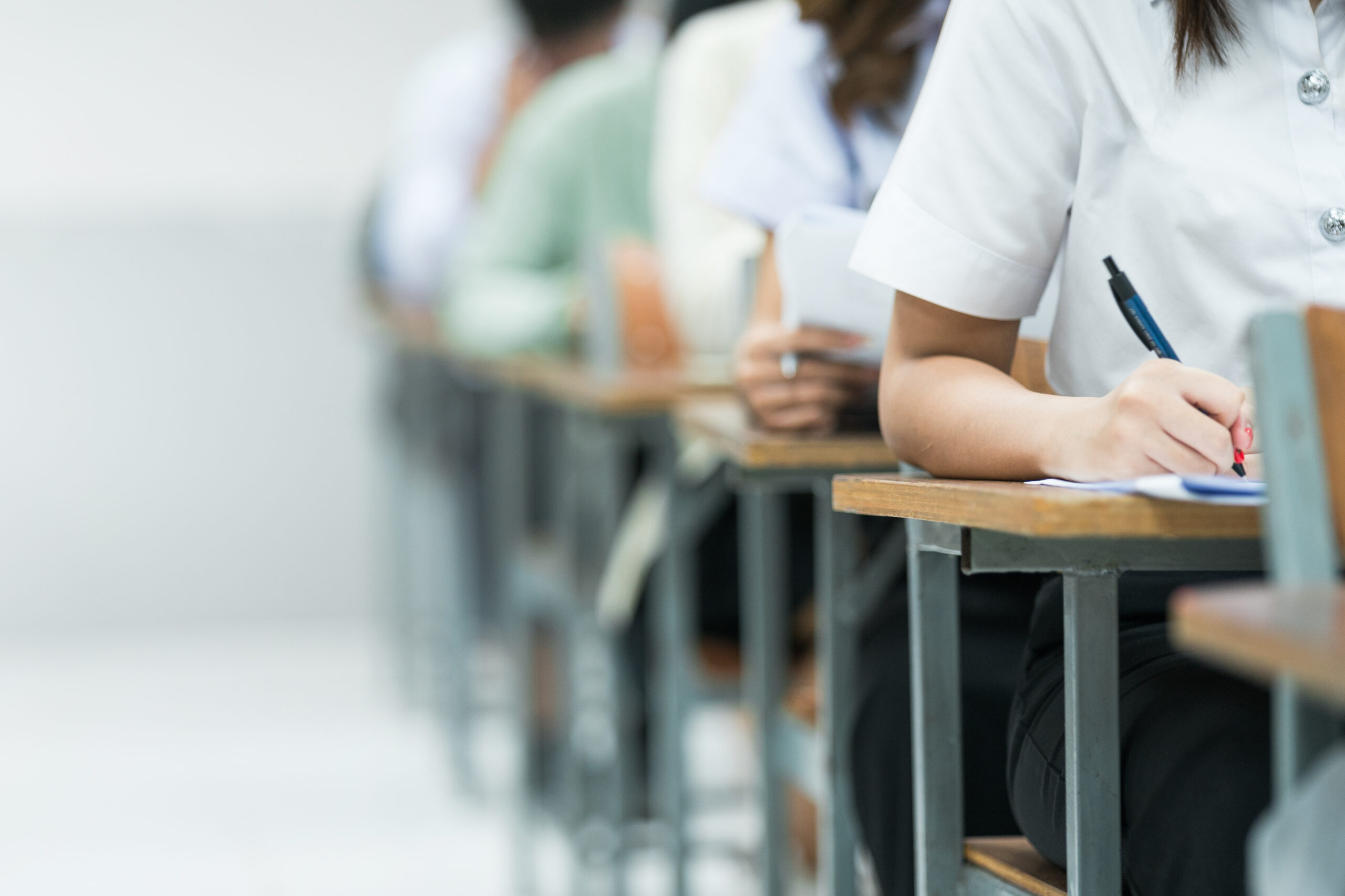 Students Taking Exam in Classroom Setting. Students in uniforms are seated in a classroom, writing answers during an exam, highlighting focus and academic testing.