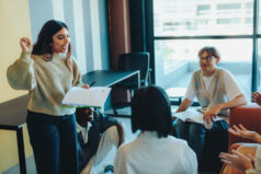 A student confidently presents a project to classmates in a modern classroom environment, with an engaged and attentive audience.