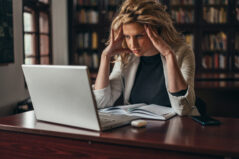 Young tired blonde faculty member using a laptop while working on her academic publication