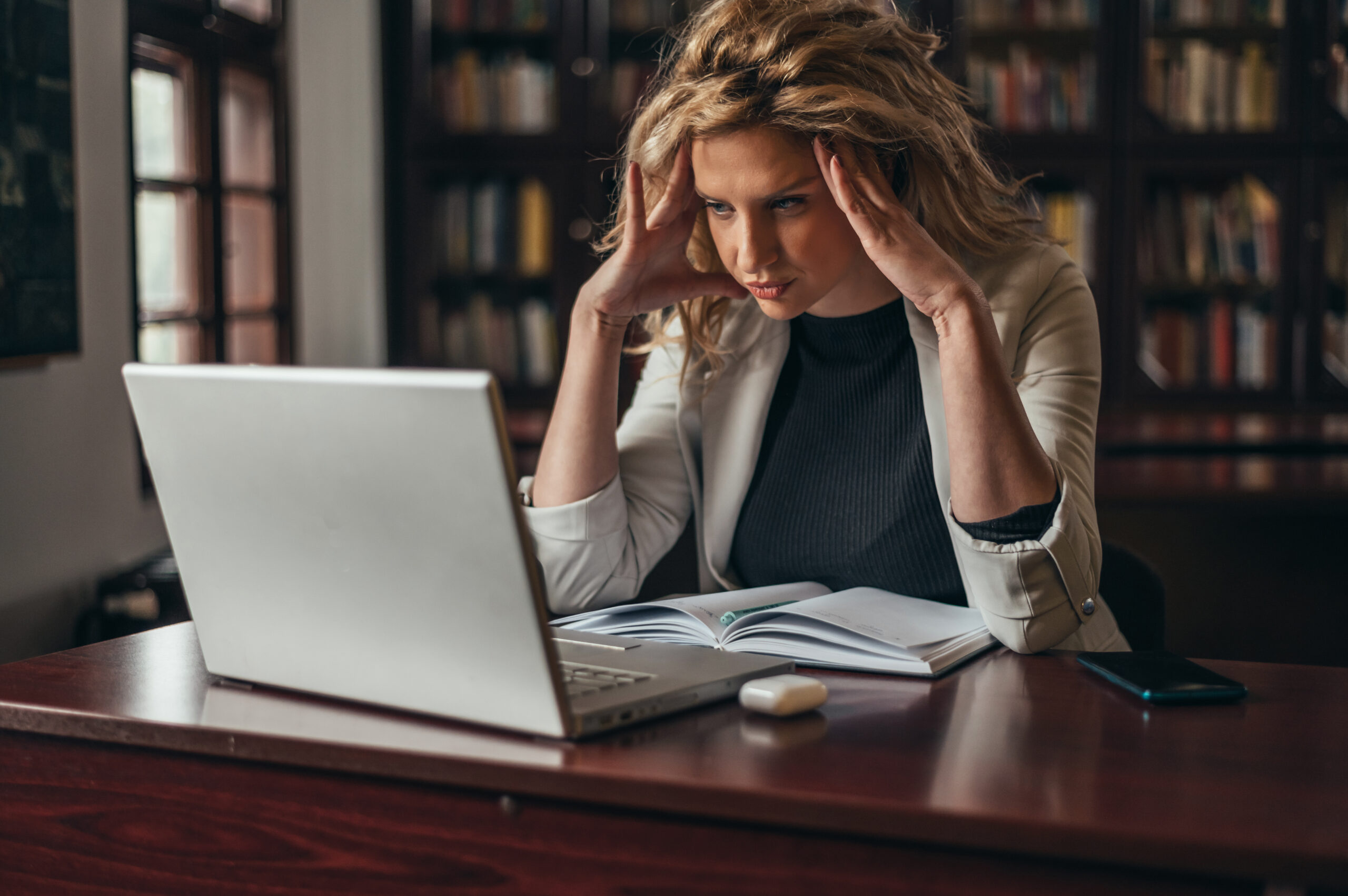 Young tired blonde faculty member using a laptop while working on her academic publication