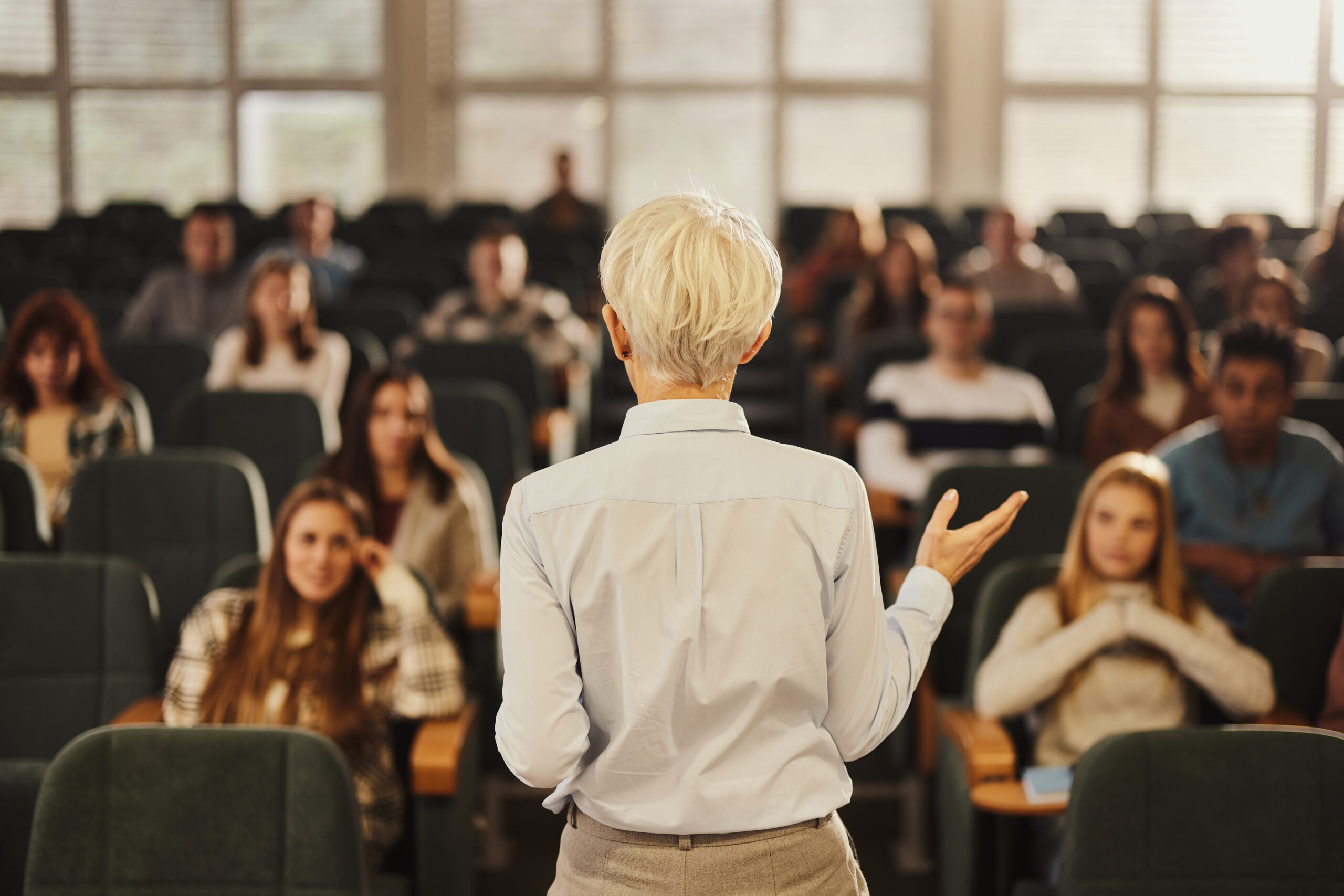 Rear view of a female professor giving a lesson to large group of her students in amphitheater.