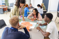 Educator engaging fellow educators at a table, directing group activities during onboarding. Showcases her collaborative approach and effective leadership onboarding educators.