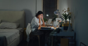 Young Asian woman student working late on laptop with stress and exhaustion in bedroom at home at night. Online education concept.